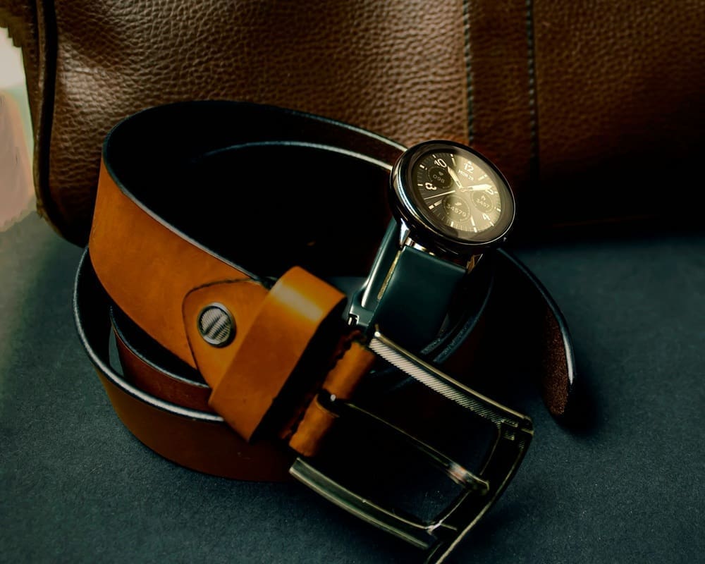 A wristwatch placed inside a coiled brown leather belt, with a brown leather bag in the background.