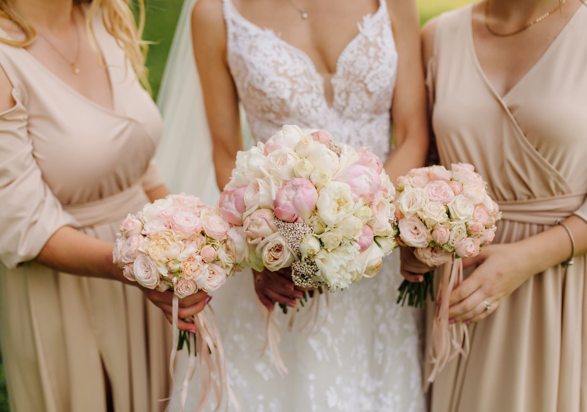 Three women in beige and white dresses holding pink and white rose bouquets, with only their torsos and hands visible.