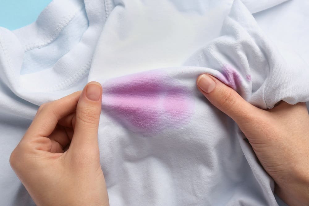 Close-up of hands holding a white t-shirt with a noticeable purple stain on the fabric.
