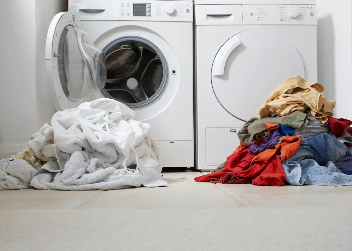 Two piles of laundry, one white and one colored, are placed in front of a washing machine and dryer on a tiled floor.