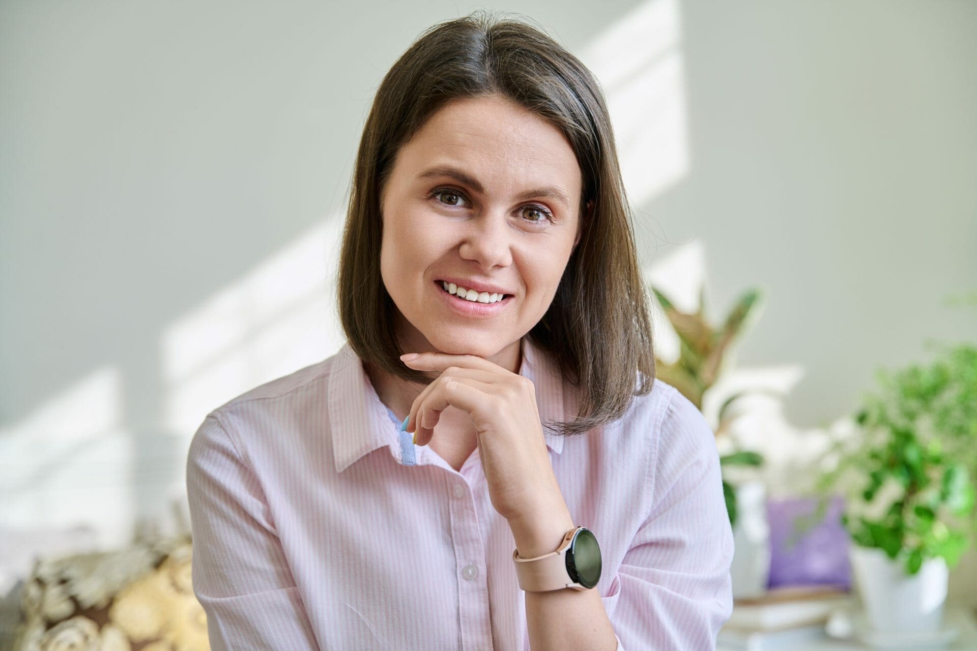 A woman in a pink shirt is sitting in front of a plant.