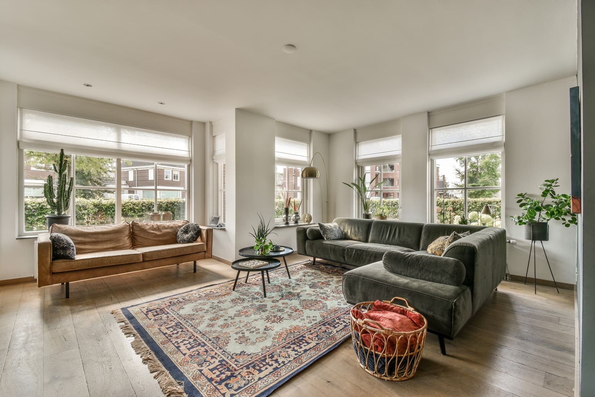 Spacious living room with two sofas, a large rug, a round coffee table, and plants by windows. Natural light fills the space.