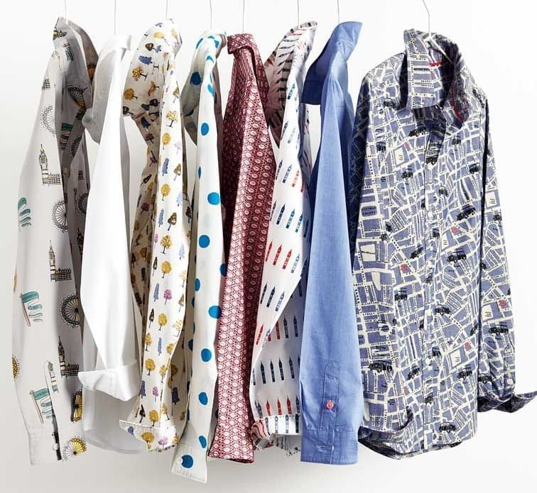 Seven patterned and plain long-sleeve shirts hang on hangers against a white background, featuring various prints and colors.